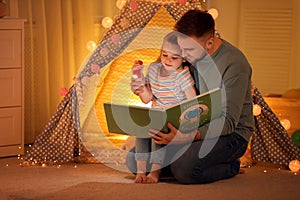 Father and daughter with flashlight reading book