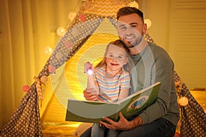 Father and daughter with flashlight reading book