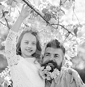Father and daughter on happy faces hugs, sakura background. Child and man with tender pink flowers in beard, wreath on