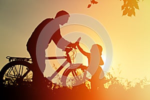 Father and daughter having fun riding bike at sunset, active family sport