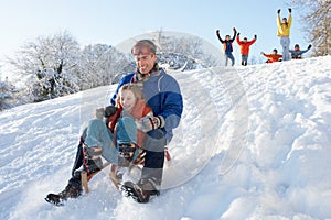 Father And Daughter Having Fun Sledging Down Hill