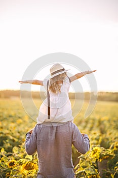 Father and daughter having fun in the sunflower field and playing. Rear view. Closeup