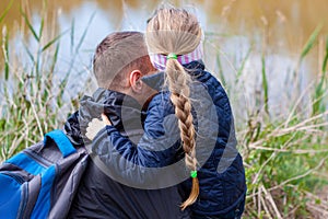 Father and daughter hugging sitting by the lake with nature lanscape. Little blond girl with braid hair walking with dad