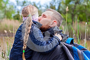 Father and daughter hugging sitting by the lake with nature lanscape. Little blond girl with braid hair walking with dad