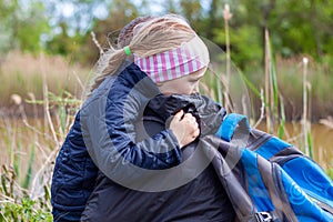 Father and daughter hugging sitting by the lake with nature lanscape. Little blond girl with braid hair walking with dad