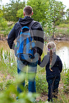 Father and daughter hugging sitting by the lake with nature lanscape. Little blond girl with braid hair walking with dad