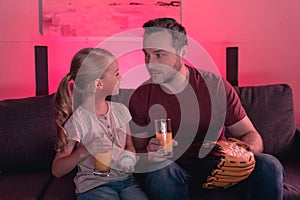 Father and daughter looking at each other and holding glasses with juice baseball mitt