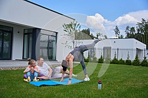 Father and daughter looking at mother doing flexibility exercise on green yard