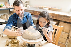 Father And Daughter Making Design On Clay Using Sculpting Tools