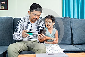 Father and daughter online shopping by using credit card payment on mobile phone at home - concept of relationship