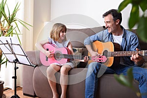 Father daughter playing guitar looking at each other with complicity