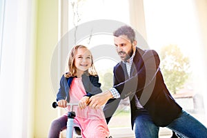 Father and daughter playing together, riding a bike indoors