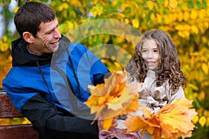 Father and daughter portrait in an autumn park. Happy people pose against the background of beautiful yellow trees. They sit on a