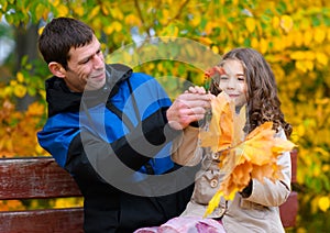 Father and daughter portrait in an autumn park. Happy people pose against the background of beautiful yellow trees. They sit on a