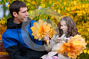 Father and daughter portrait in an autumn park. Happy people pose against the background of beautiful yellow trees. They sit on a