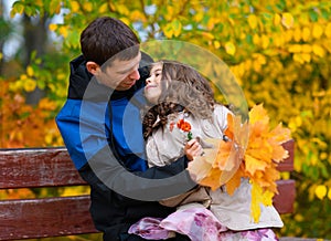 Father and daughter portrait in an autumn park. Happy people pose against the background of beautiful yellow trees. They sit on a