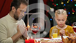 Father and daughter praying before Christmas dinner, uphold christian traditions