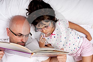 Father and daughter reading a book in bed
