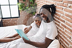Father and daughter reading book sitting on bed at bedroom