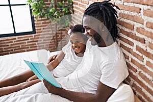 Father and daughter reading book sitting on bed at bedroom