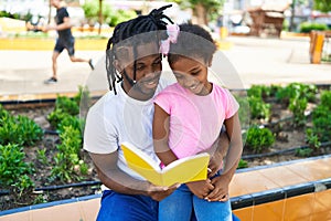 Father and daughter reading book sitting together on bench at park