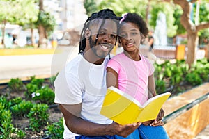 Father and daughter reading book sitting together on bench at park