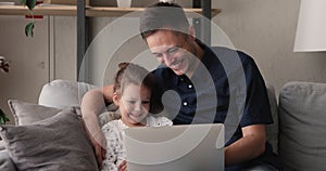 Father and daughter relaxing on couch with laptop watching cartoons