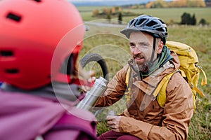 Father and daughter resting, having snack during hiking together in autumn mountains.