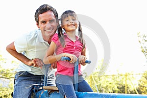 Father And Daughter Riding On See Saw In Playgroun