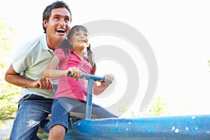 Father And Daughter Riding On See Saw In Playgroun