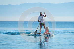 Father and daughter riding SUP stand up paddle on vacation