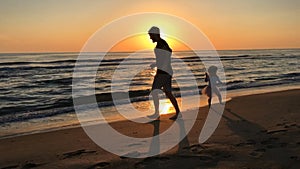 Father and daughter run along the beach at sunset.