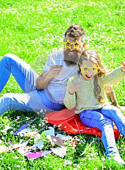 Father and daughter sits on grass at grassplot, green background. Child and dad posing with star shaped eyeglases photo