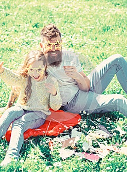 Father and daughter sits on grass at grassplot, green background. Child and dad posing with star shaped eyeglases photo