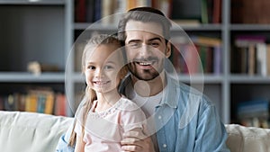 Father and daughter sitting on couch smiling looking at camera