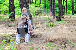 Father and daughter are sitting in the park with a laptop, a bright summer photo with free space