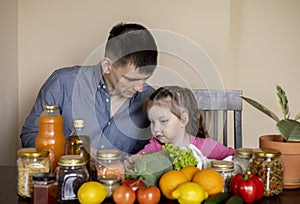 Father and daughter are sitting at the table in the kitchen. Fresh products bought in the store