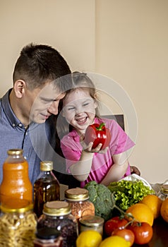 Father and daughter are sitting at the table in the kitchen. Fresh products bought in the store