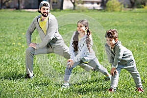 father with daughter and son doing physical exercise on grassy meadow