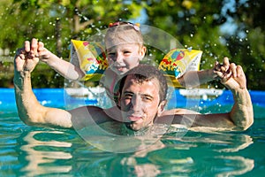 Father and daughter swim in pool. Girl riding on man. She swims in pillows.