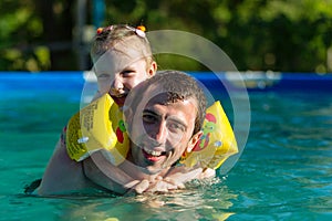 Father and daughter swim in pool. Girl riding on man. She swims in pillows.