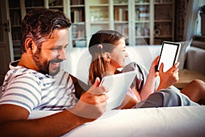 Father and daughter using digital tablet in living room