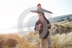 Father And Daughter Walking Through Dunes On Winter Beach