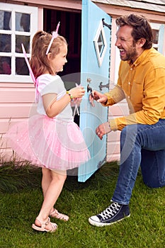 Father With Daughter Wearing Fairy Costume Playing Outdoors In Garden By Playhouse