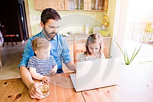 Father and daughters, playing on laptop, sitting in kitchen