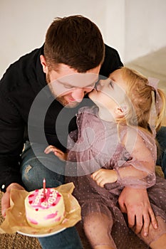 Father and dauther celebrates the birthday of their little daughter. Birthday celebration in dresses with cake.