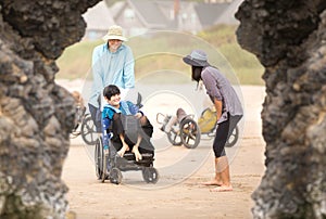 Father and disabled son in wheelchair on beach with family