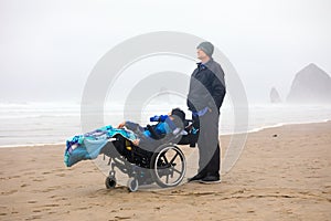 Father with disabled son in wheelchair on cold foggy beach