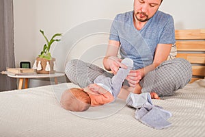 Father dresses a newborn in the bedroom. Clothes baby undershirts and sliders on a baby close-up and copy space. Home care and bab