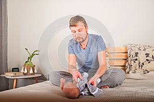 Father dresses a newborn in the bedroom. Clothes baby undershirts and sliders on a baby close-up and copy space. Home care and bab